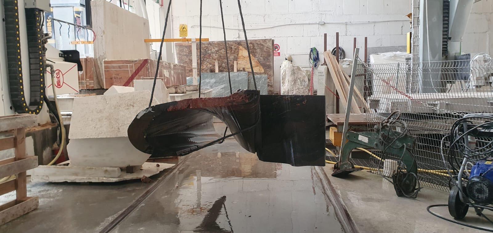 Peça de pedra suspensa horizontalmente por cabos no interior da fábrica.